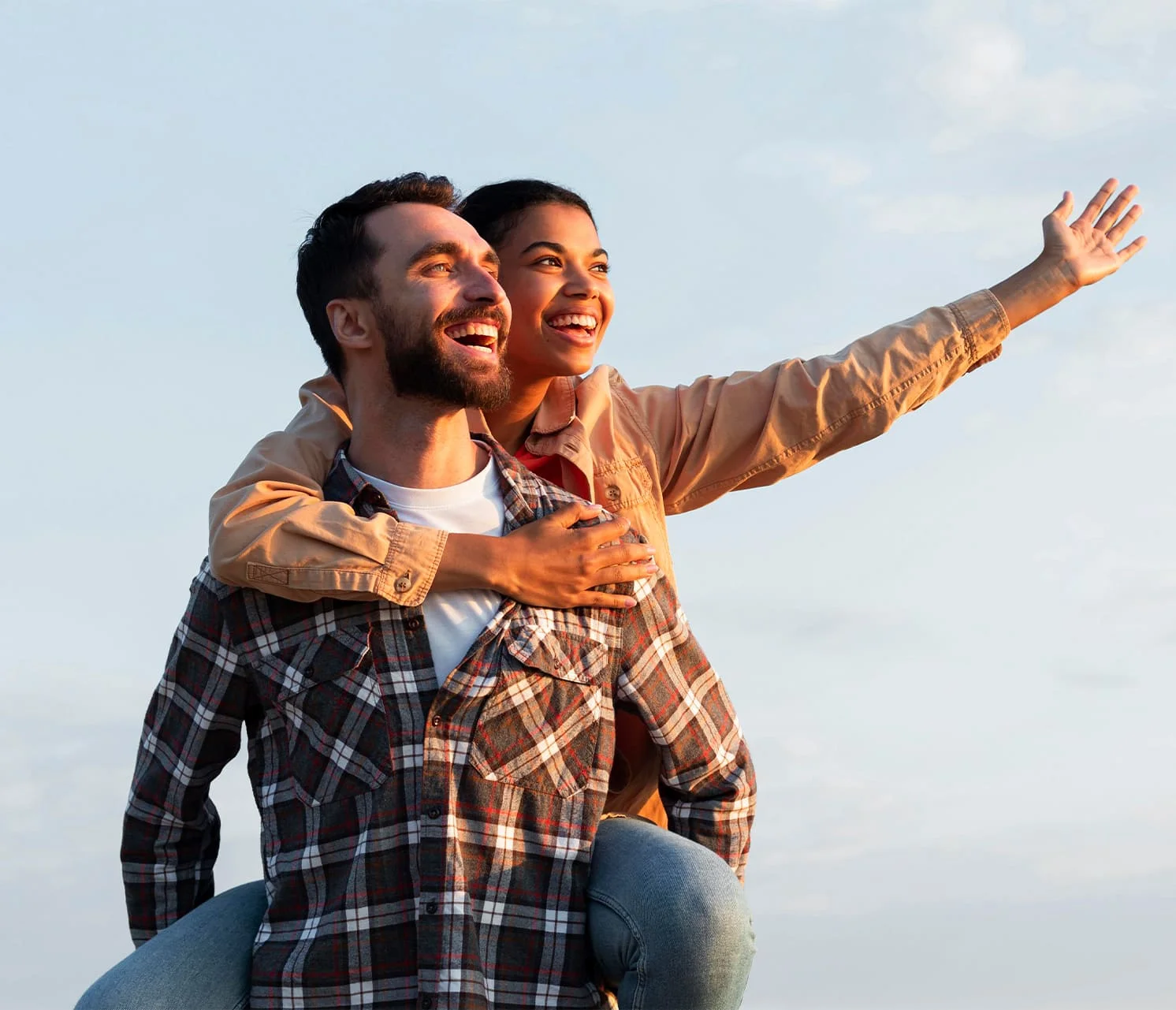 Smiling young man carrying a woman on his back with her hand up